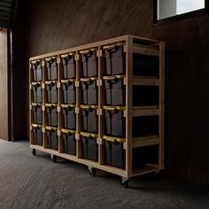 a large wooden shelf filled with lots of black bins and yellow tape on wheels