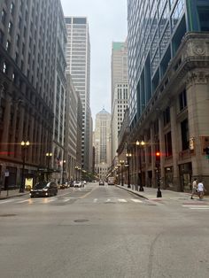 an empty city street with tall buildings and traffic lights on both sides in the distance