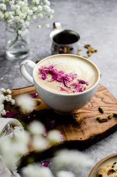 a cup of coffee with pink flowers in it on a wooden tray next to some cookies