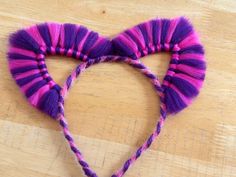 a pair of purple and pink ears on top of a wooden table next to yarn