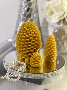 three yellow pine cones sitting on top of a table next to a crystal vase filled with flowers