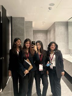 four women standing in a bathroom taking a selfie with their cell phone and notebooks