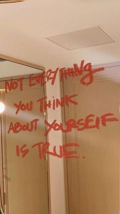 a bathroom mirror with graffiti written on the wall and below it is a light that reads, not everything you think about yourself is true