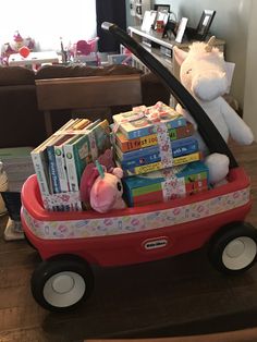 a red wagon filled with lots of books on top of a wooden floor next to a white teddy bear