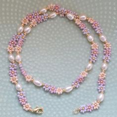 a pink and white beaded necklace on a blue surface with a gold charm hanging from it's end