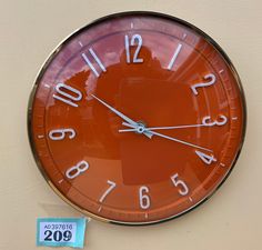 an orange clock hanging on the side of a wall with a price tag next to it