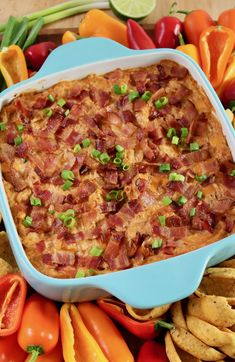 a blue casserole dish filled with bacon and green onions surrounded by tortilla chips