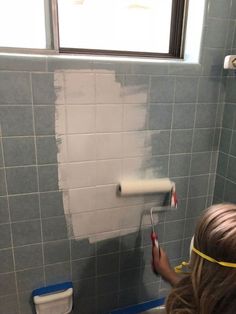 a woman is using a roller to paint the wall in a bathroom with blue tiles