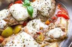 a pan filled with meat and vegetables covered in sauce, garnished with fresh herbs