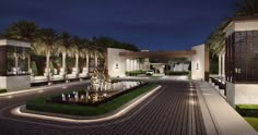 the entrance to a luxury home at night with palm trees and water fountain in front