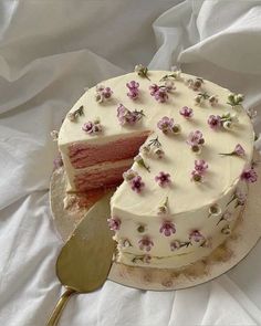 a cake with white frosting and pink flowers on it is being cut by a knife