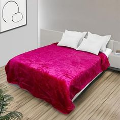 a bed with a pink blanket on top of it next to a potted plant