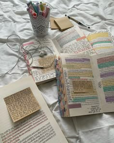 an open book sitting on top of a bed next to some pens and pencils