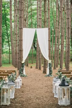 an outdoor wedding setup with white drapes and lanterns, greenery and flowers on the aisle