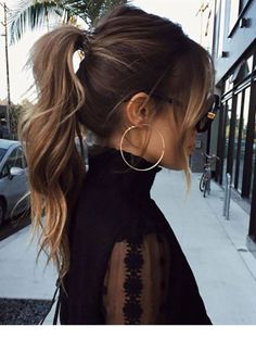 a woman with long hair wearing large hoop earrings and black sheer top on the street