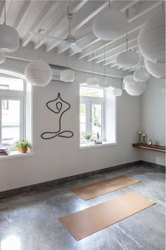 two yoga mats are on the floor in front of three windows with paper lanterns hanging from them