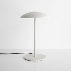 a white table lamp sitting on top of a white counter next to a black cord