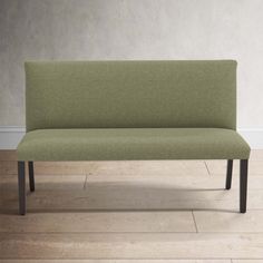 a green couch sitting on top of a hard wood floor next to a white wall