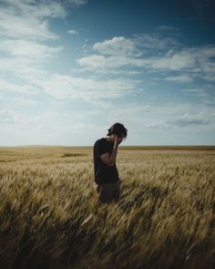 a woman standing in a wheat field talking on a cell phone while holding her head to her ear