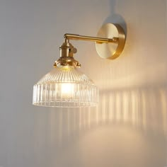 a light that is on the side of a white wall with a glass shade hanging from it