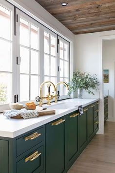 a kitchen with green cabinets and white counter tops, gold faucets on the sink