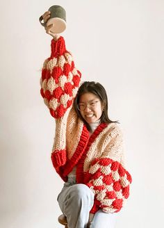 a woman sitting on top of a stool holding a cup in her hand and smiling