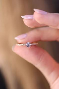 a woman's hand holding a diamond ring in her left hand, with the middle finger touching it