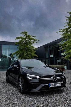 a black mercedes cla is parked in front of a building with trees and bushes