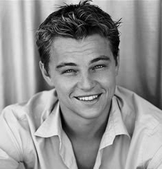 a black and white photo of a man with short hair smiling at the camera, wearing a button up shirt