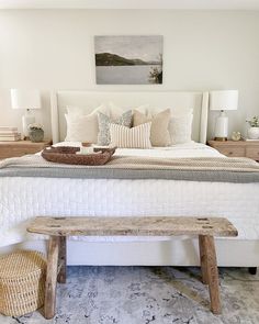 a bed with white sheets and pillows in a bedroom next to a basket on the footboard