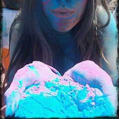 a woman with blue and pink powder on her face is holding something in her hands