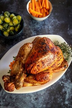 a whole chicken on a plate with carrots and brussel sprouts