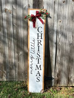 a wooden sign that says christmas and has a red bow on it in front of a fence