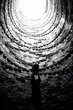 a black and white photo of a person standing in the middle of a brick tunnel