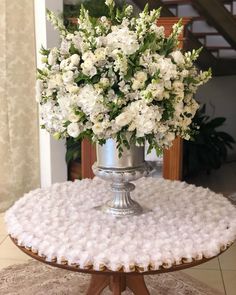 white flowers are in a silver vase on a round table with a rug underneath it