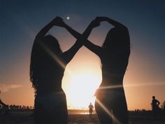 two women standing in front of the sun with their arms around each other's shoulders