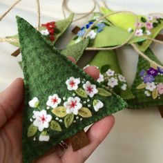 someone is holding two felt ornaments in their hands, one has flowers on it and the other has leaves