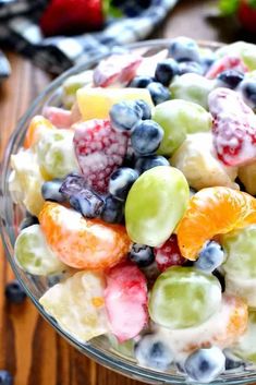 a glass bowl filled with fruit salad on top of a wooden table