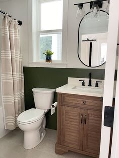 a white toilet sitting next to a sink in a bathroom under a window with a shower curtain