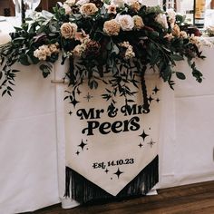 a wedding sign with flowers and greenery on the front is hanging from a white table cloth