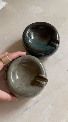 a hand holding a small bowl next to a larger bowl on the floor with another one in it