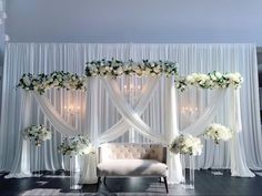 a couch sitting in front of a white curtain covered wall with flowers and candles on it