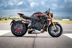 a black and red motorcycle parked on top of a tarmac with clouds in the background