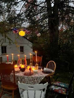 a table with candles on it in front of a white house and some wooden chairs