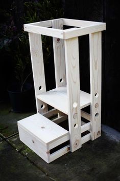 a wooden step stool sitting next to a potted plant on the ground in front of a black wall