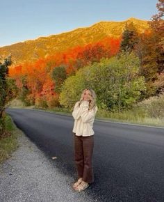 a woman standing on the side of a road with her head in her hands and mountains in the background