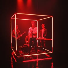 two men standing in front of a red light on stage with guitars and drums behind them