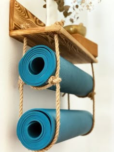 two blue yoga mats are hanging on the wall next to a wooden shelf with rope