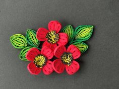 four red flowers with green leaves on a gray surface, one is made out of plastic