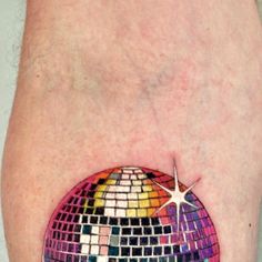 a colorful disco ball tattoo on the left thigh and right leg, with a star in the center